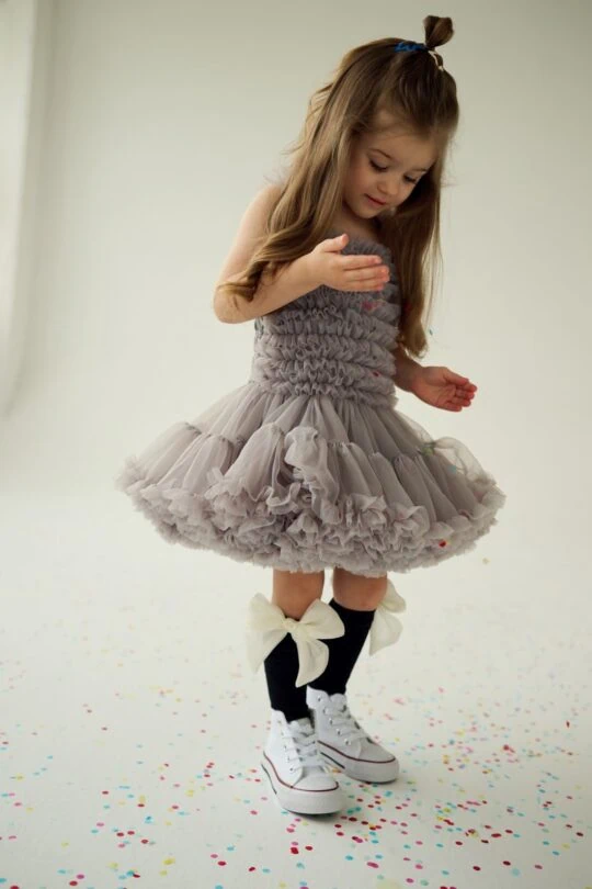 Little girl playing with her gray tulle dress and black knee socks with white sneakers