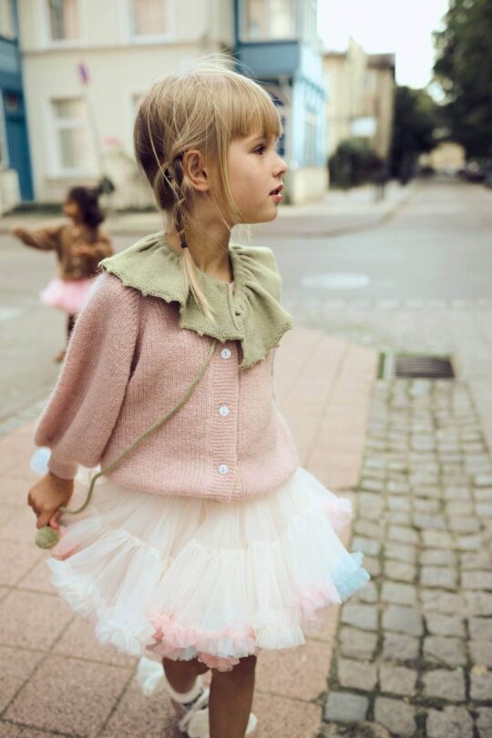 Niña con cuello decorativo de lana, jersey de punto rosa y falda de tul blanco