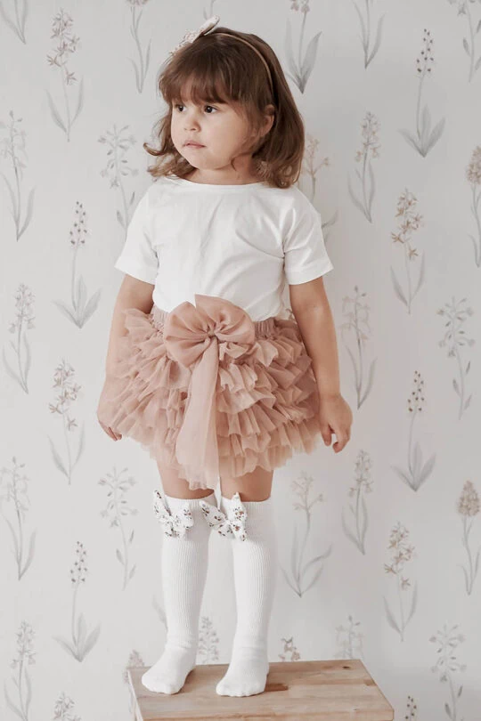 Niña con pantalón corto rosa con volantes y calcetines blancos de niña con lazo de mariposa