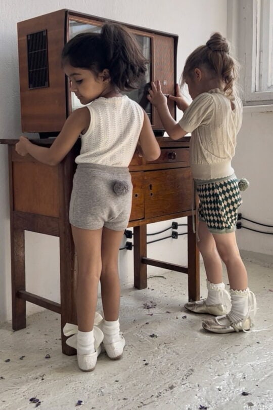 Niña con pantalón corto gris de niña, calcetines blancos por la rodilla y top blanco juega con la tele