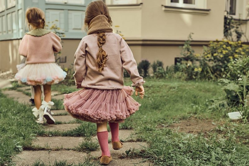 Dziewczynki w białej spódnicy tiulowej z falbankami w kolorach tęczy dip-dye oraz dziewczynka w fioletowej spódniczce tutu. Obydwie mają dziane sweterki i szaliki