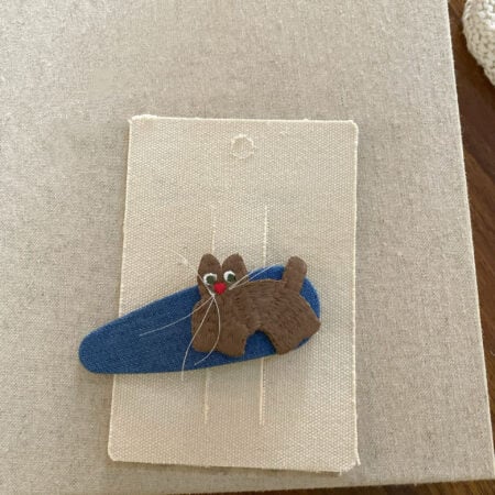 Haarnadel für ein Mädchen mit einer gestickten braunen Katze auf blauem Hintergrund.