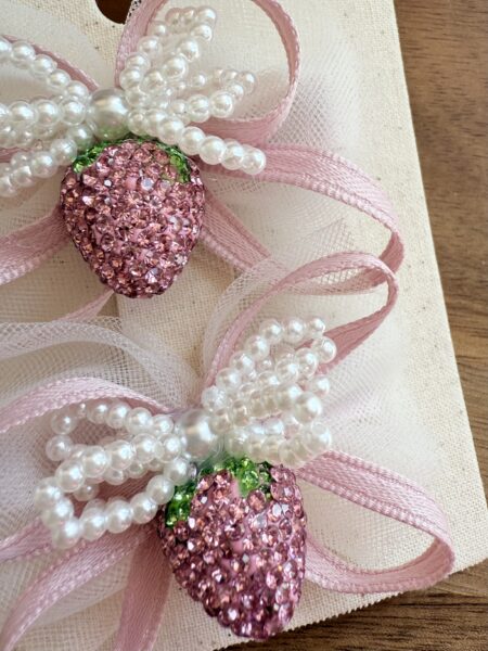 Un set di fermagli per bambina con una fragola rosa con cristalli e un fiocco, decorato con perline.
