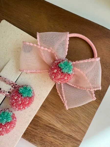 Pasador de pelo para niñas con lazo rosa y motivo decorativo de fresas.
