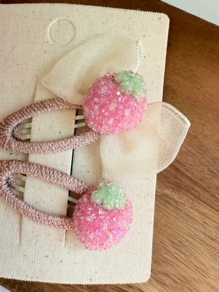 Hair frills for girls in pink with a strawberry-shaped decoration and a small bow.