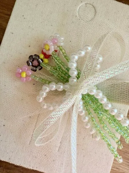 Floral brooch made of beads in shades of pink, green and white, decorated with pearl accents.