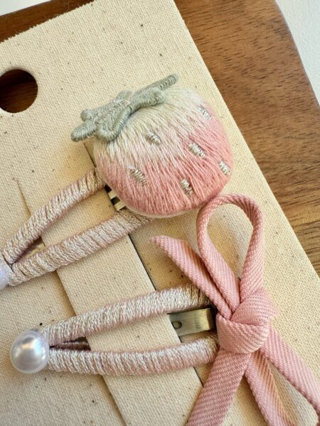 Anstecknadeln für ein Mädchen: eine 3D-Anstecknadel in Form einer Erdbeere in Rosa und Mint und eine rosa Schleife.
